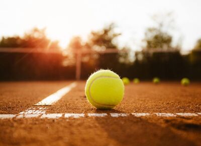 Detailaufnahme eines Tennisballes, welcher auf dem Sportplatz liegt.