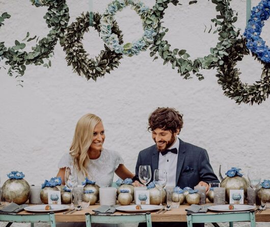 Das Hochzeitspaar lacht sich an während es vor der gedeckten Tafel sitzt in der Hochzeitslocation Gut Ising am Chiemsee.