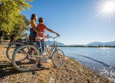 Two people stand with bicycles on the shores of Lake Chiemsee in glorious sunshine.
