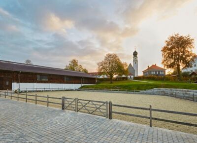 View of a riding arena of the Hotel Gut Ising at Chiemsee with a white church in the background.
