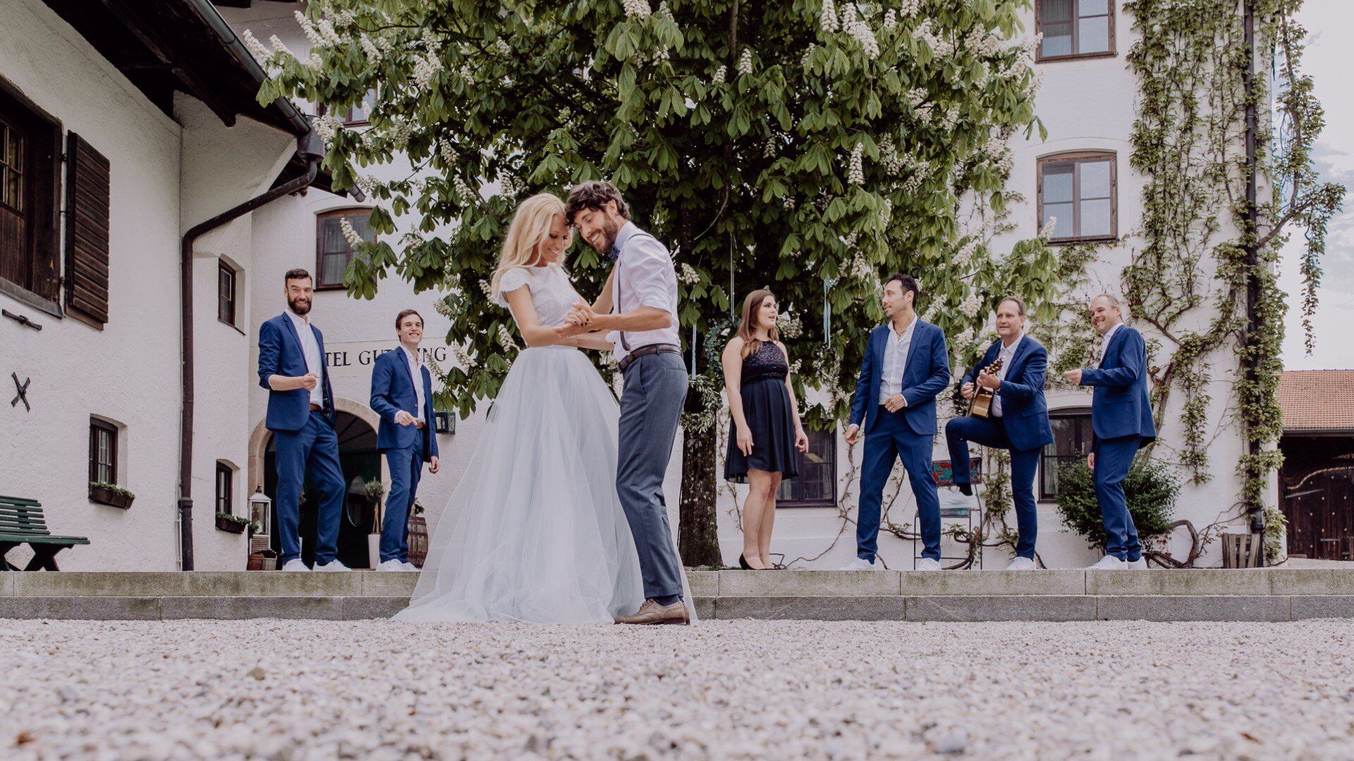 A wedding couple dances in the historic courtyard of Hotel Gut Ising on Lake Chiemsee while a band, dressed all in blue, plays music in the background.