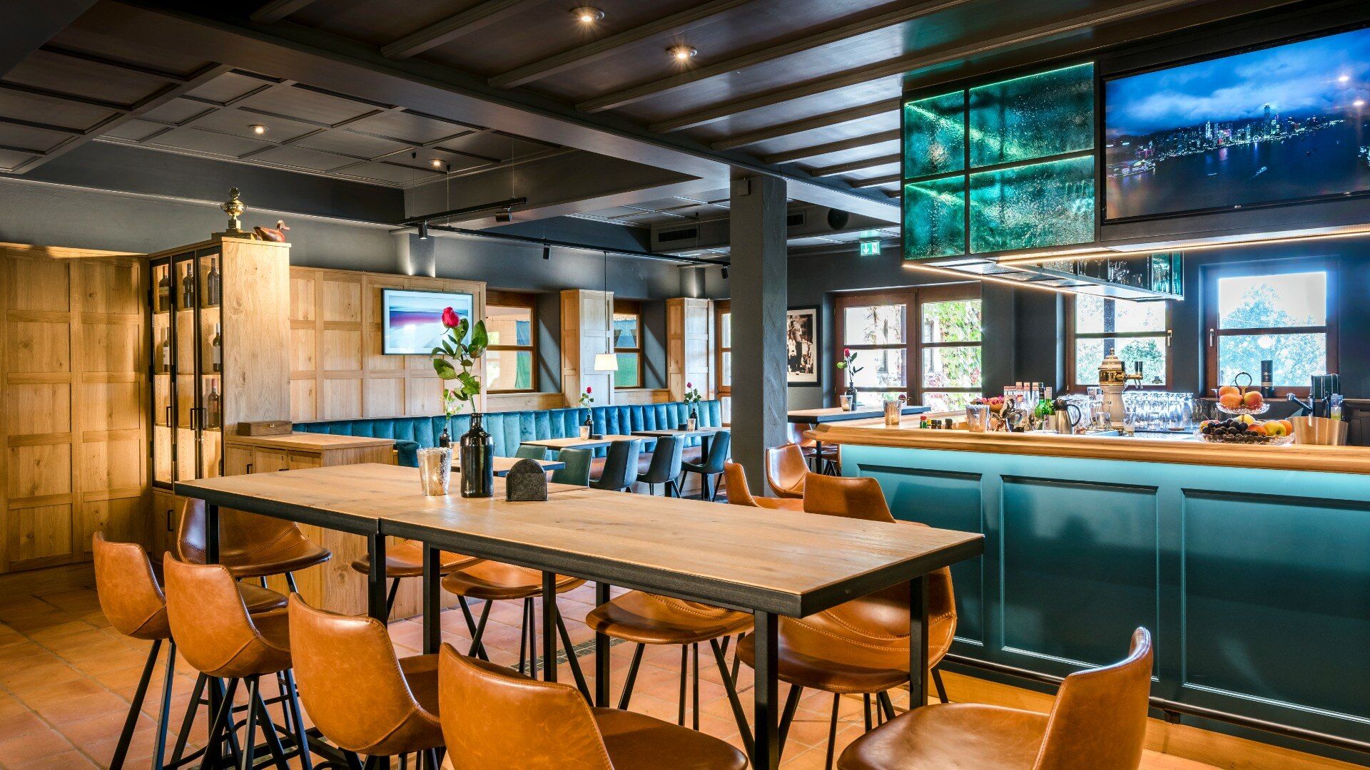 Blick über den Hochtisch auf die in Blautönen gestaltete Bar und weitere Sitzplätze im modernen Restaurant am Chiemsee