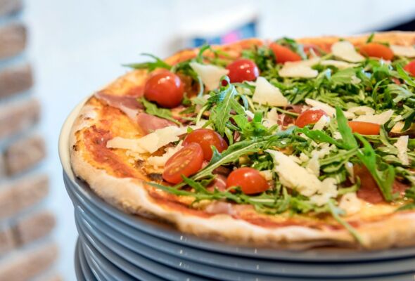Eine frisch gebackene Pizza mit Ruccola und Tomaten garniert im italienischen Restaurant Il Cavallo auf Gut Ising am Chiemsee.