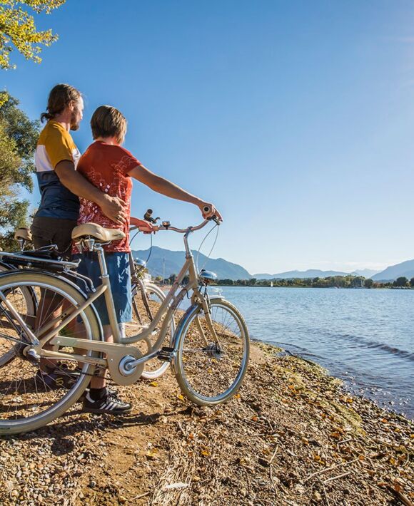 Zwei Personen stehen mit Fahrrädern an den Ufern des Chiemsees bei herrlichen Sonnenschein.