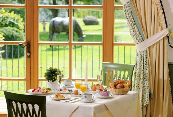 Blick in den Frühstücksraum in die Salzburger Stube des Hotel  Gut Ising am Chiemsee wo ein eingedeckter Frühstückstisch mit Blick in den Innenhof zu sehen ist.