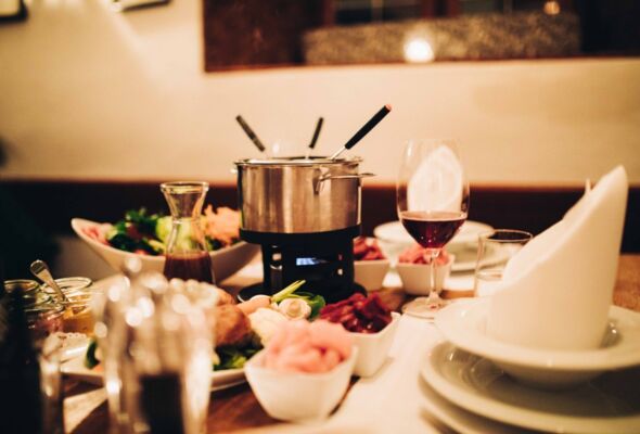 Ein Fondue Behälter steht in der Mitte eines Tisches zusammen mit weiteren Speisen im Fondue Restaurant Gut Ising am Chiemsee.